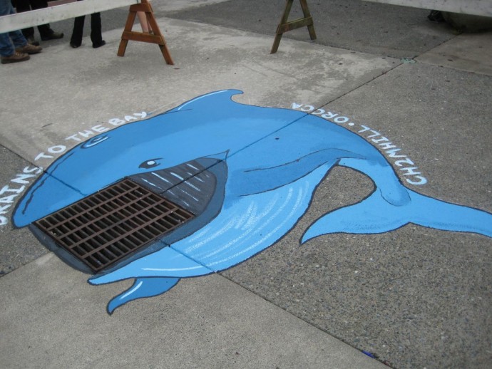 Joshann painting around a storm drain of a whale